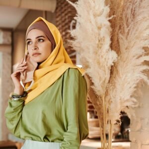 Stylish Muslim woman in vibrant hijab posing indoors with pampas grass decor.